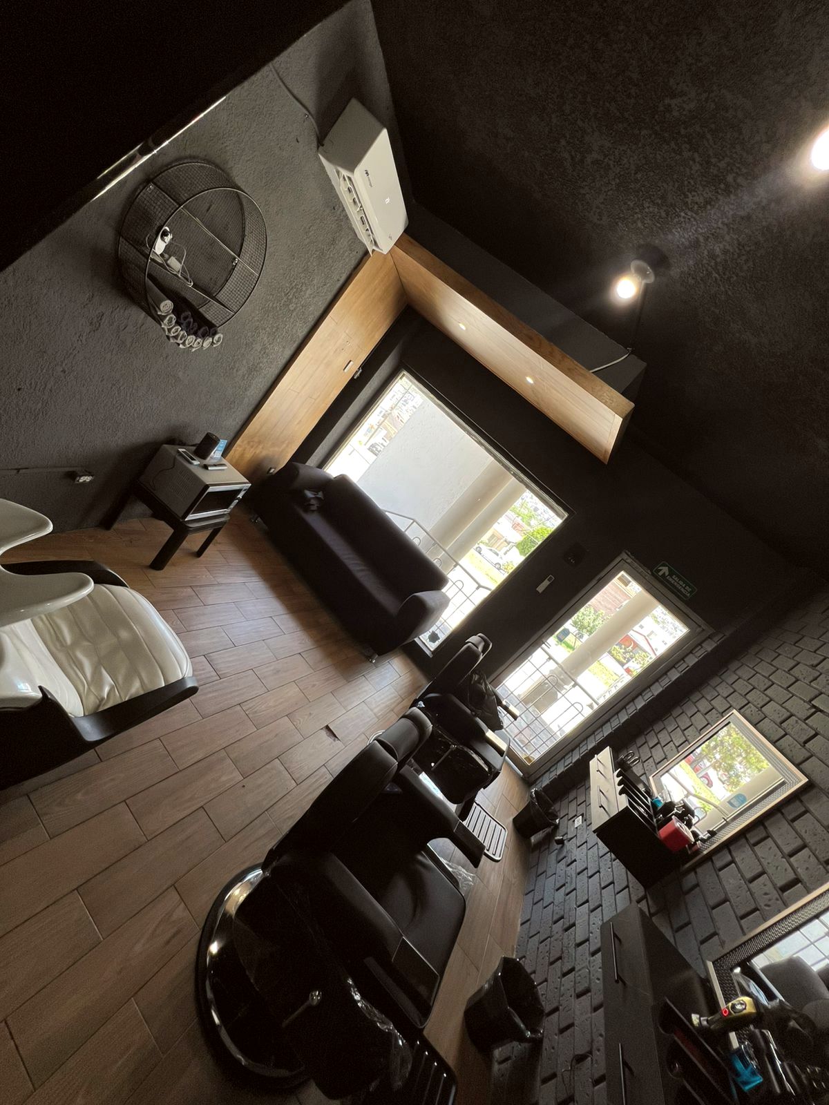 Vista superior del estudio: muros carbón, piso de madera y sillones de barbero de piel negra